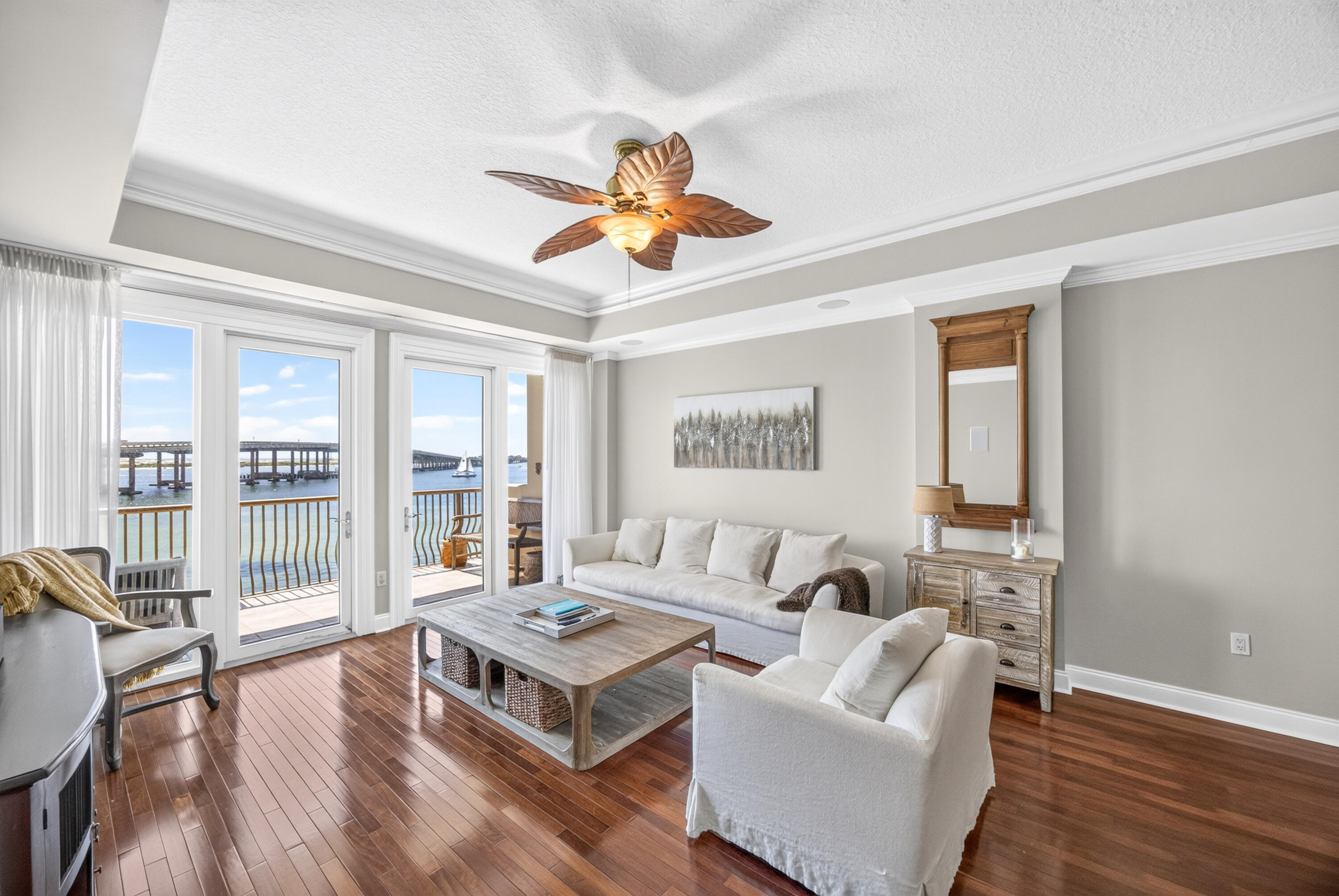 Living room with white seating and hardwood floors, opening onto a balcony with water views.