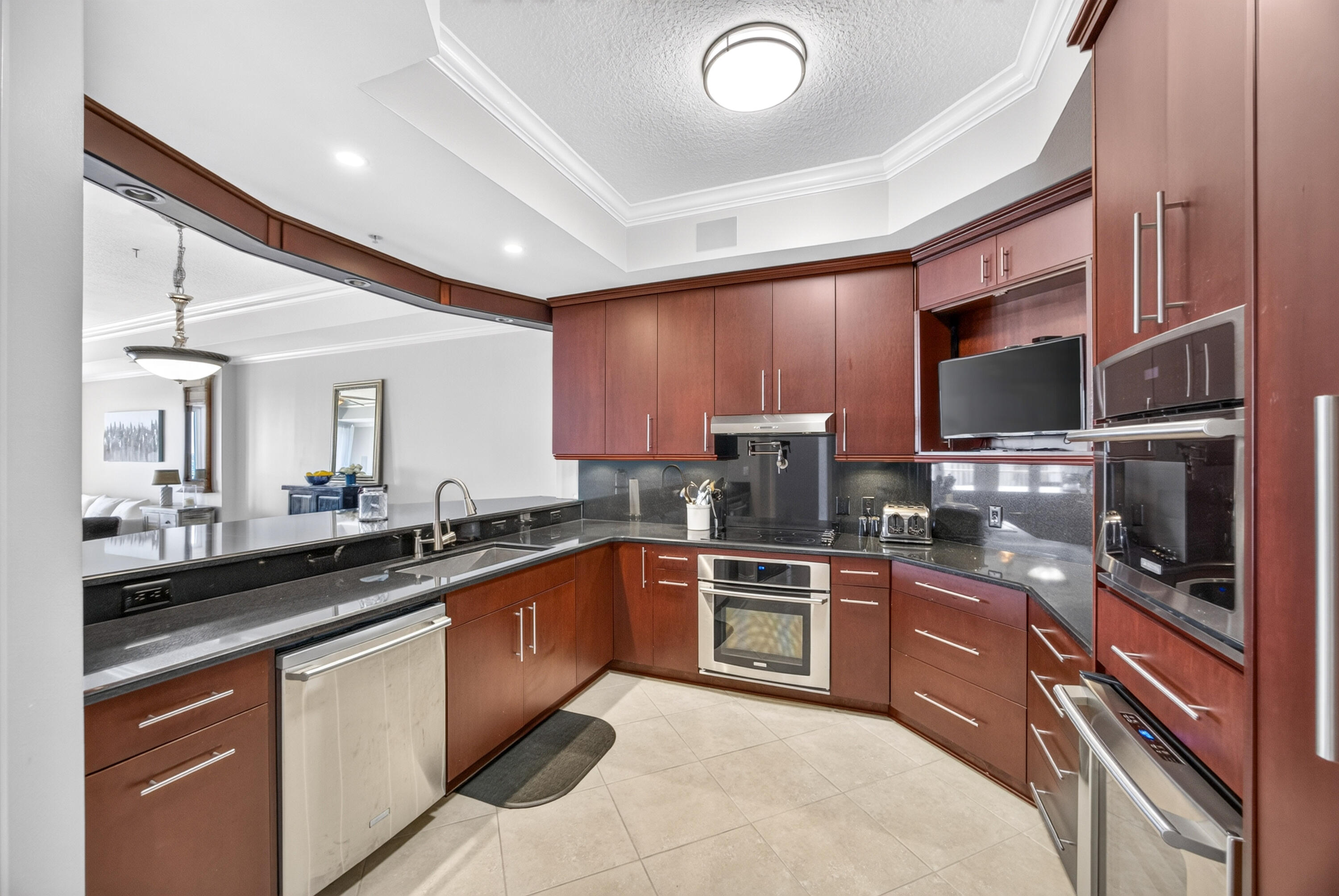 U-shaped kitchen with reddish-brown cabinets, dark stone counters, and stainless steel appliances.