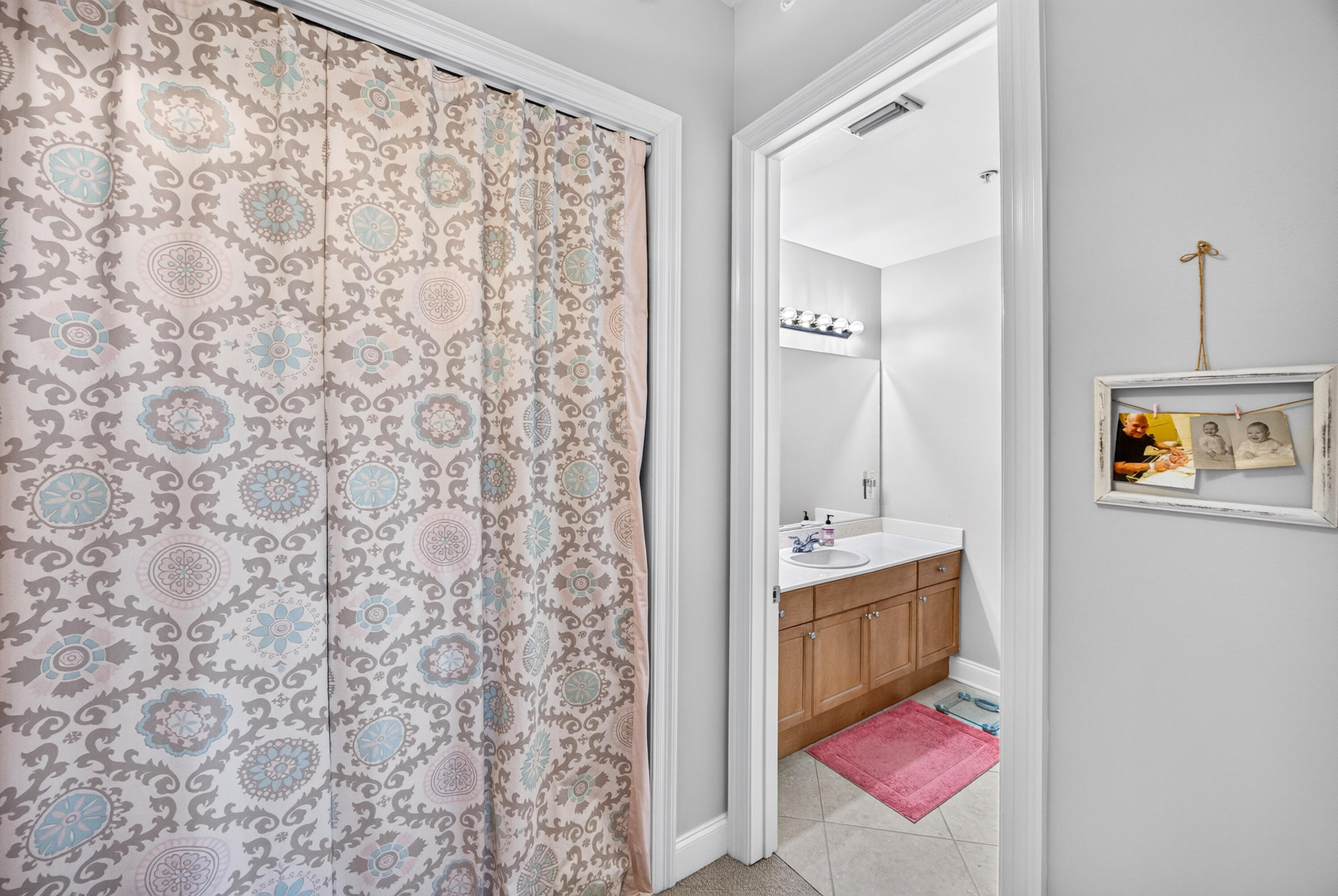 Bedroom with patterned curtain beside an open doorway to a bathroom with a wood vanity and pink bath mat.