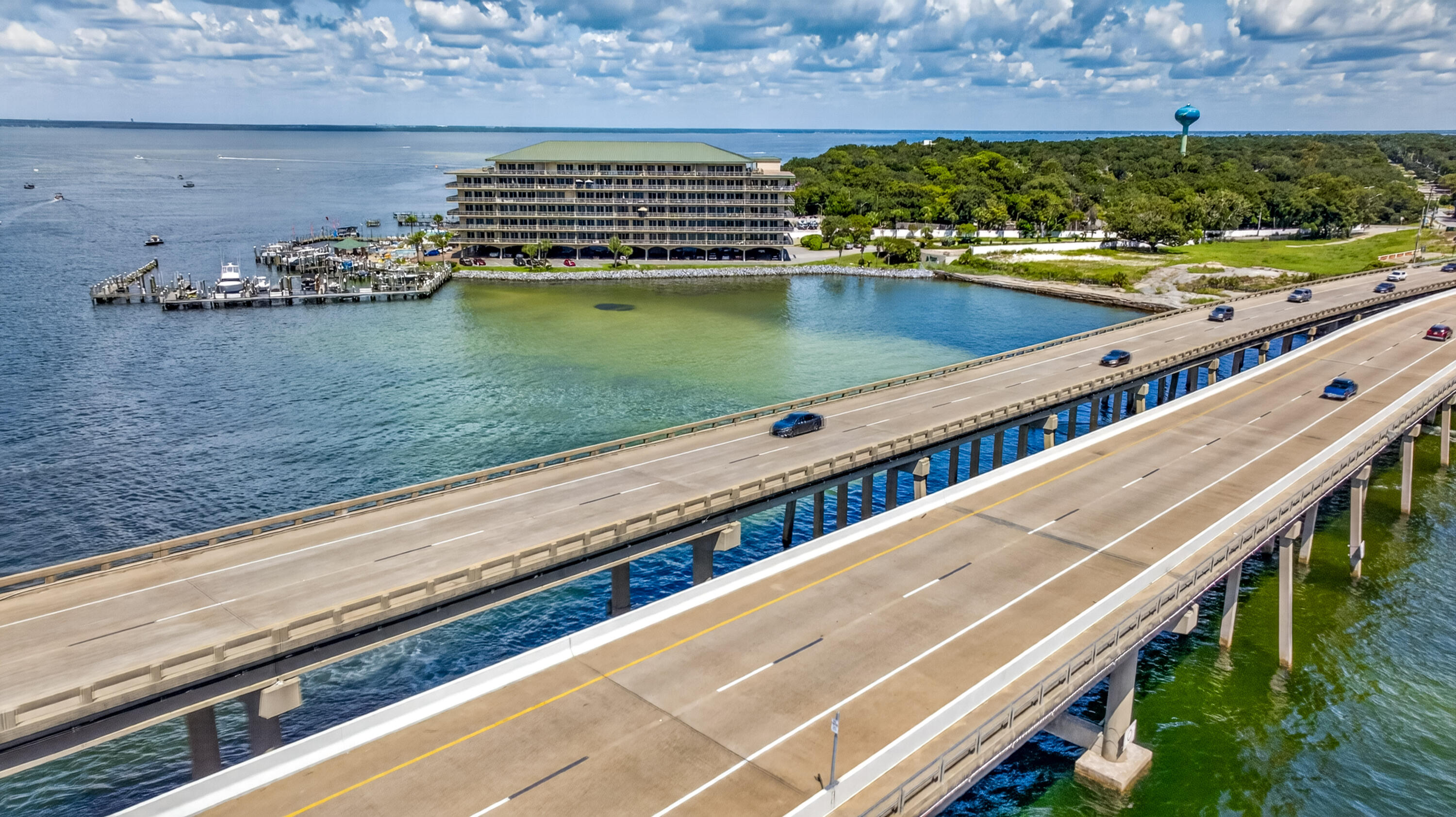 Waterfront condominium and marina beside a highway bridge crossing blue-green water.