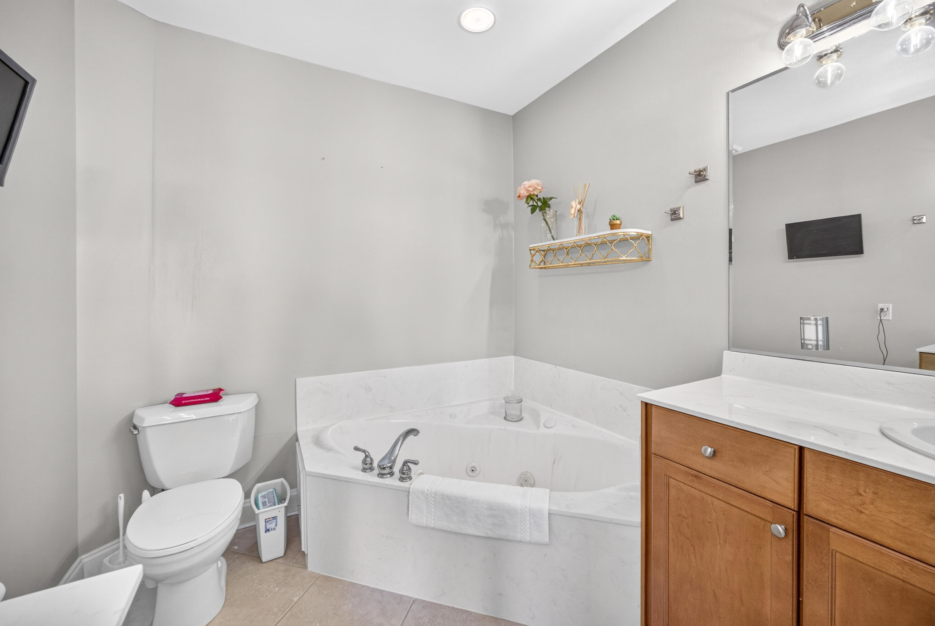 Bathroom with a corner jetted tub, toilet, and wood vanity beneath a large mirror.
