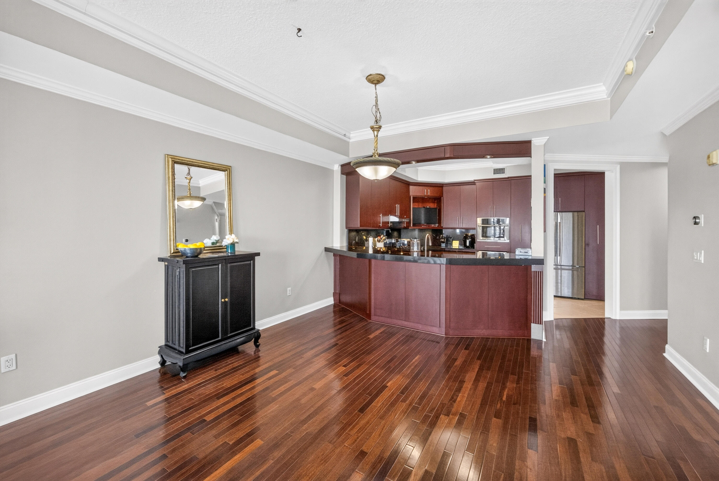 Kitchen with dark wood cabinetry, black counters, stainless appliances, and polished hardwood floors.