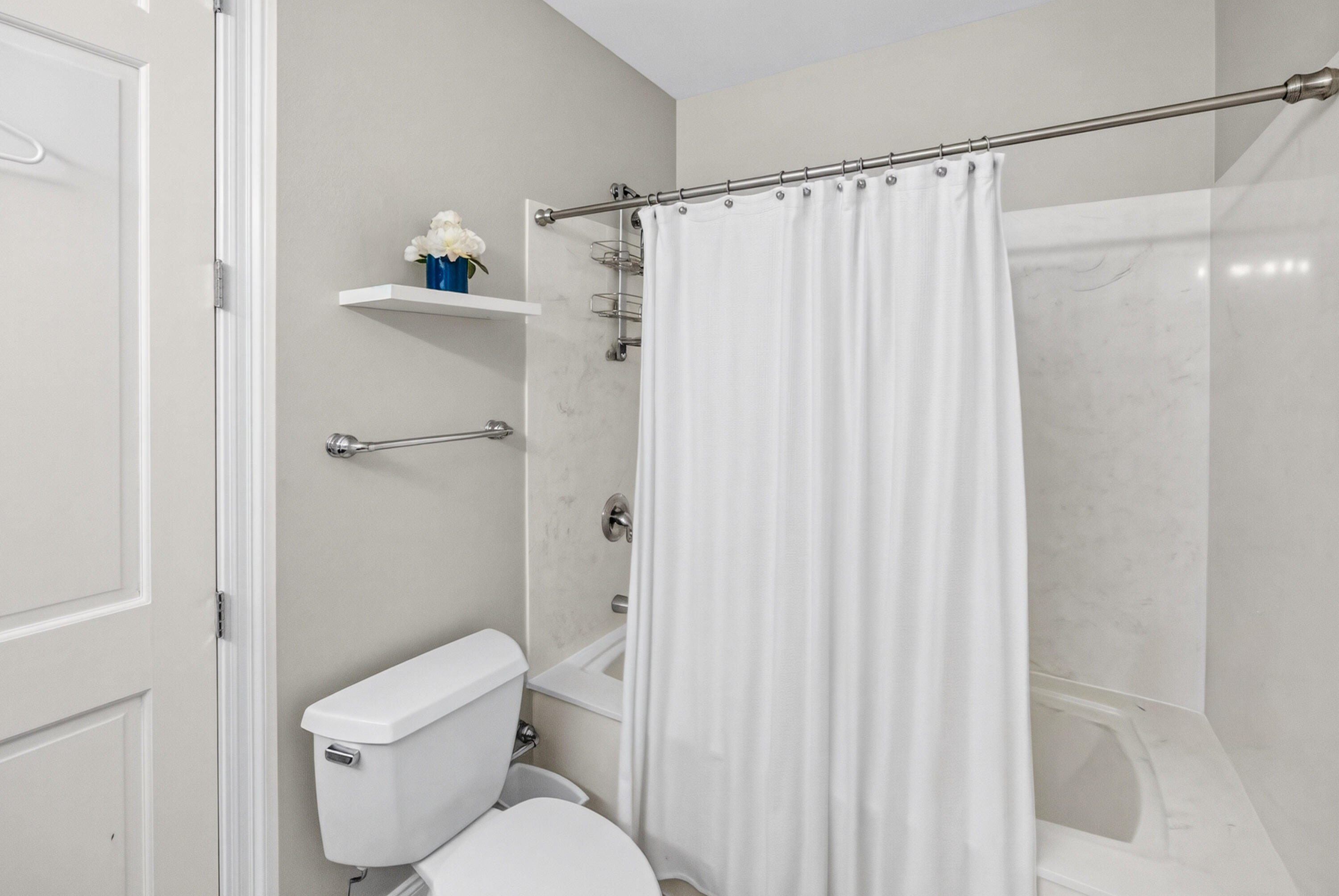 Bathroom with a white-curtained tub and shower, marble surround, chrome grab bar, and toilet.