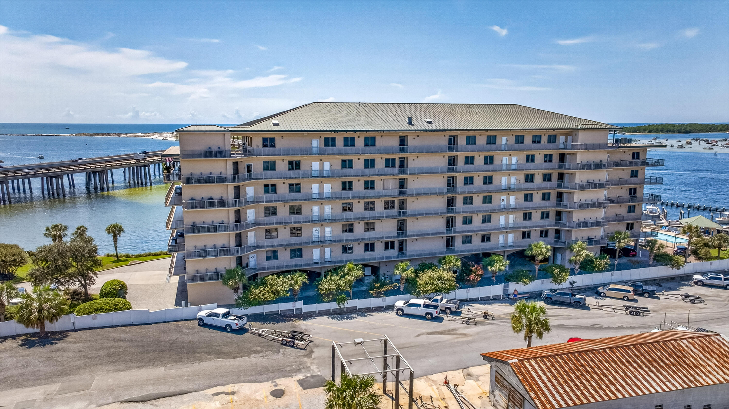 Waterfront condominium with rows of balconies, a pier, and open water behind it.