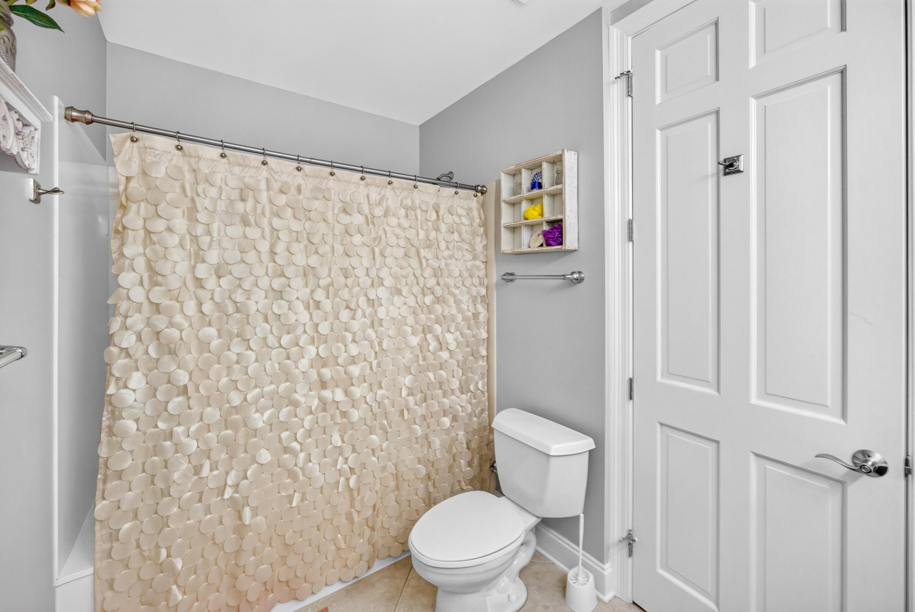 Bathroom with a beige scalloped shower curtain, white toilet, and gray walls.