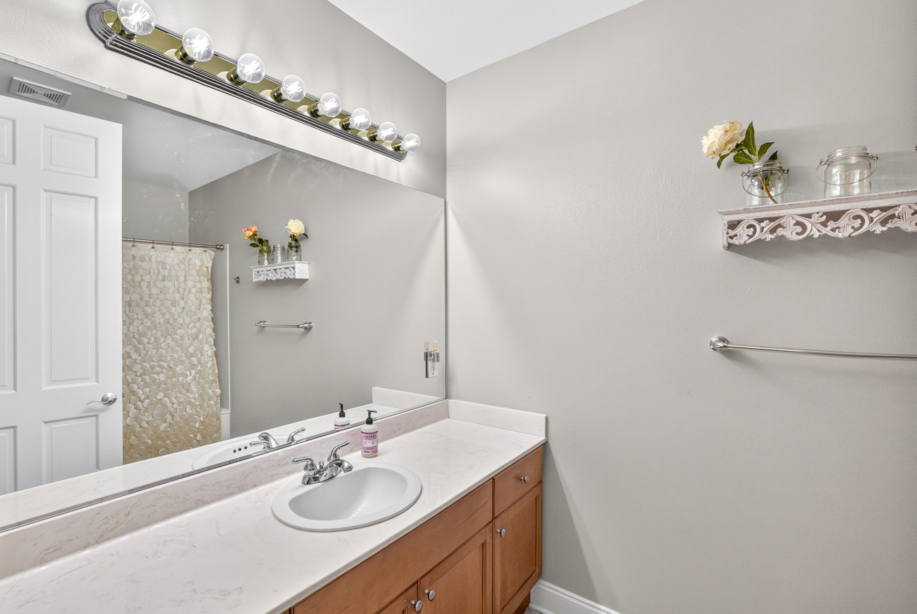 Bathroom vanity with a large mirror, globe lights, white countertop, and warm wood cabinetry.