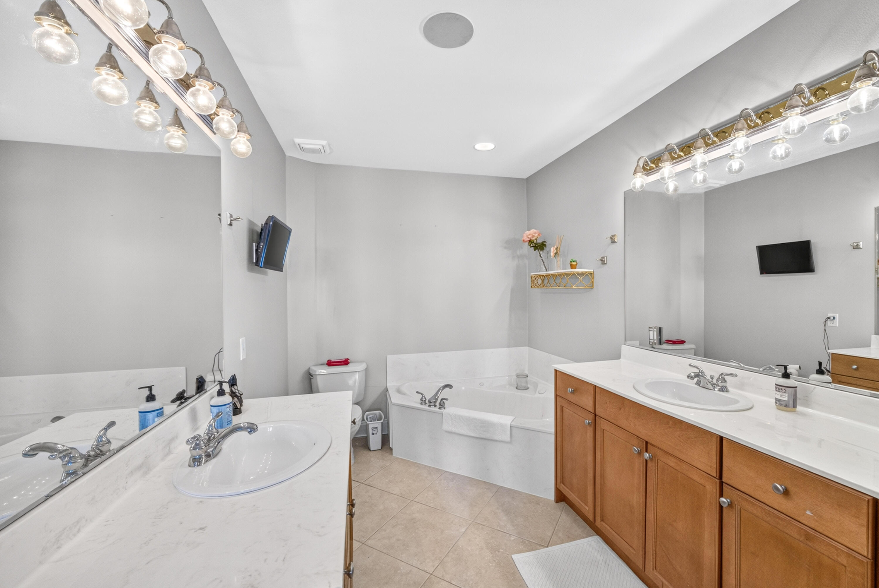 Bathroom with a soaking tub and dual vanities with wood cabinets and globe lights.