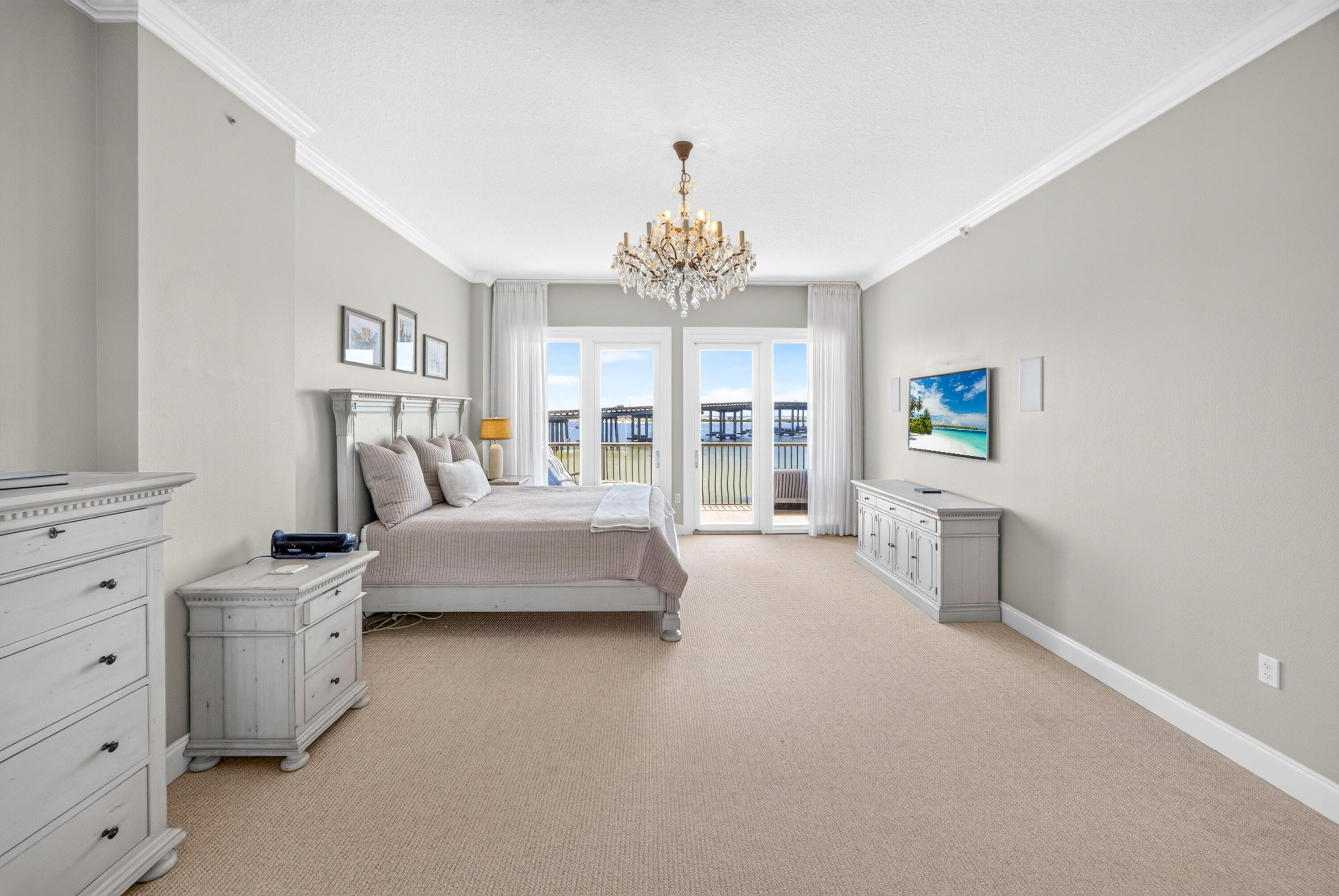 Furnished bedroom with a chandelier and balcony doors overlooking the water and bridge.