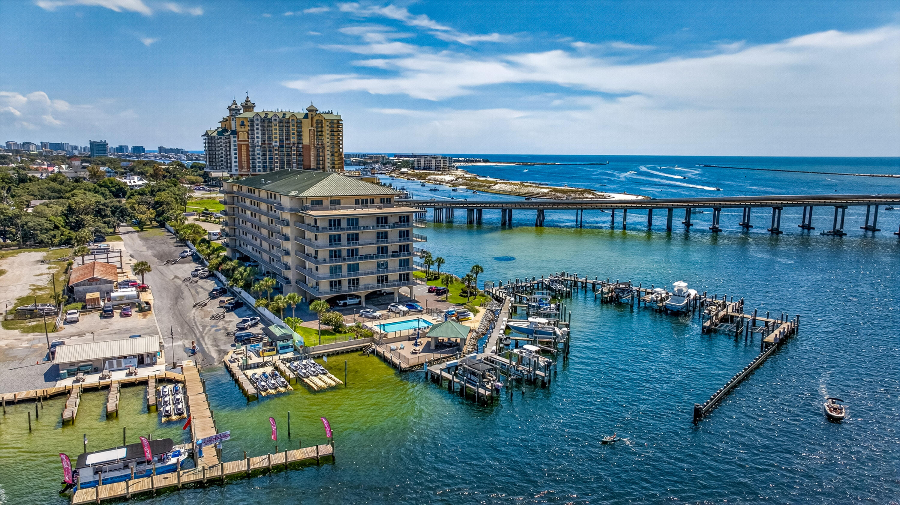 Waterfront condominium and marina with boat docks, a pool, and a bridge over blue water.