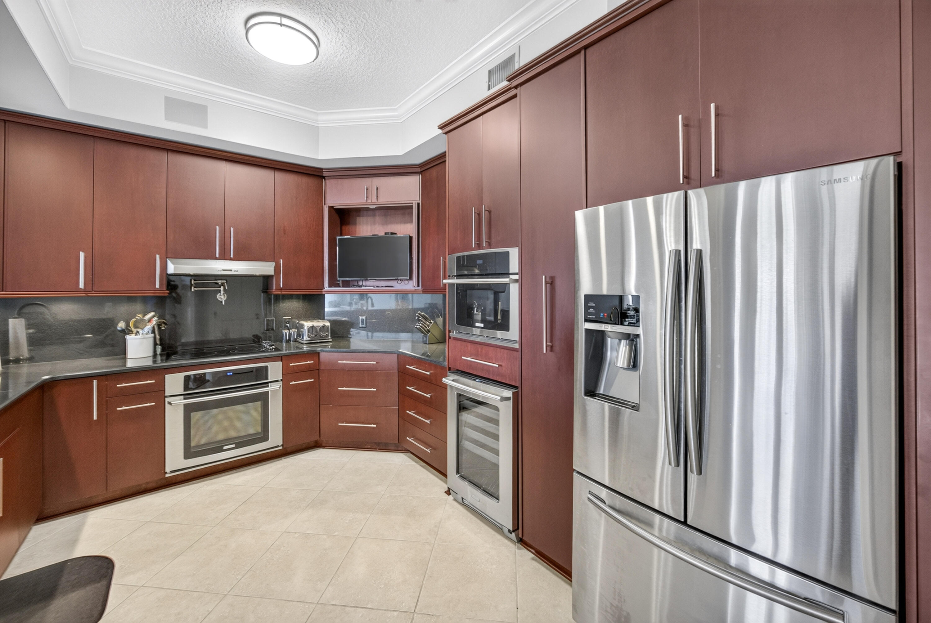 Kitchen with reddish-brown cabinets, dark countertops, and a large stainless steel French-door refrigerator.