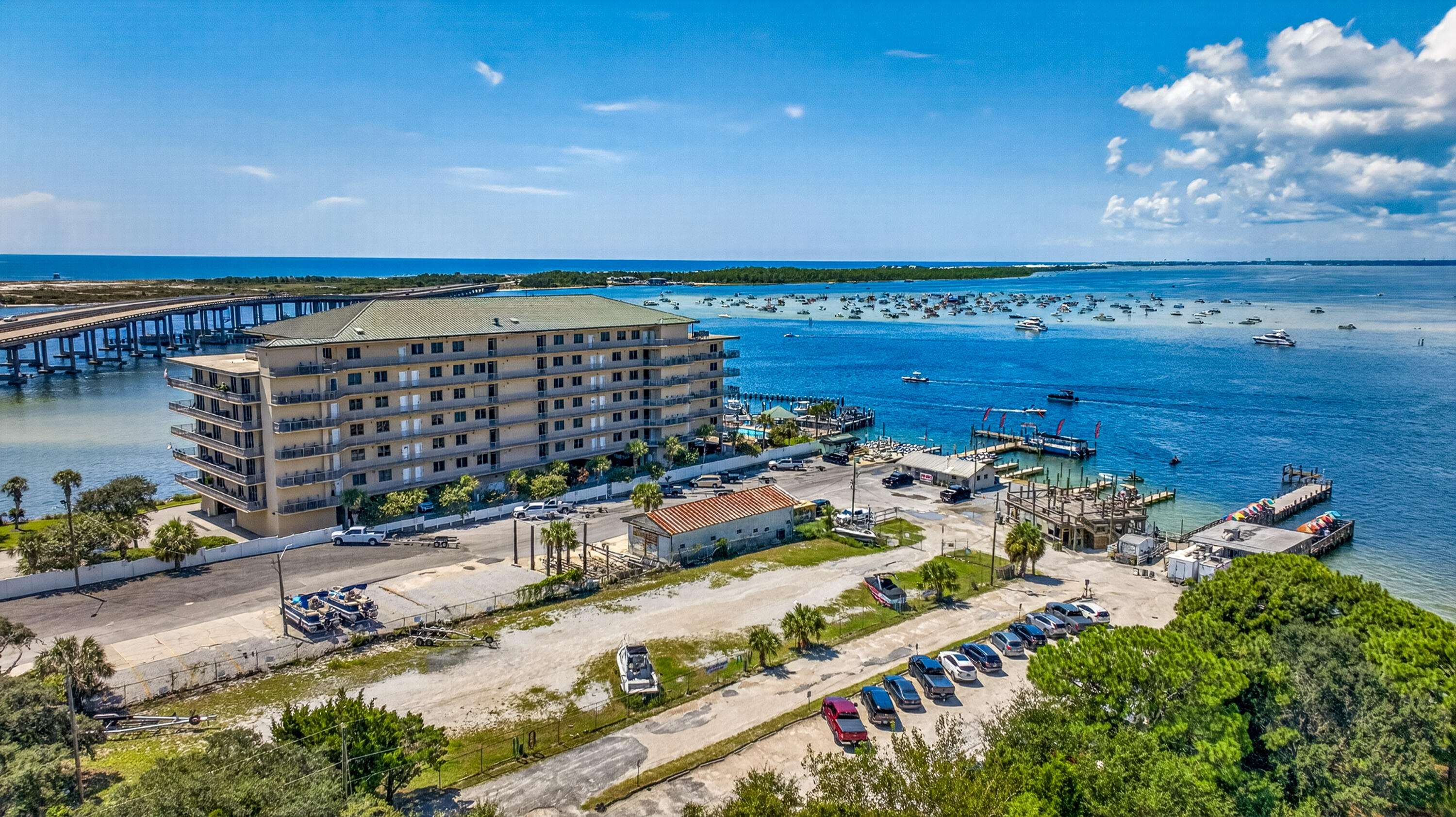 Waterfront condominium beside a marina, with boats on blue water and a bridge in the distance.
