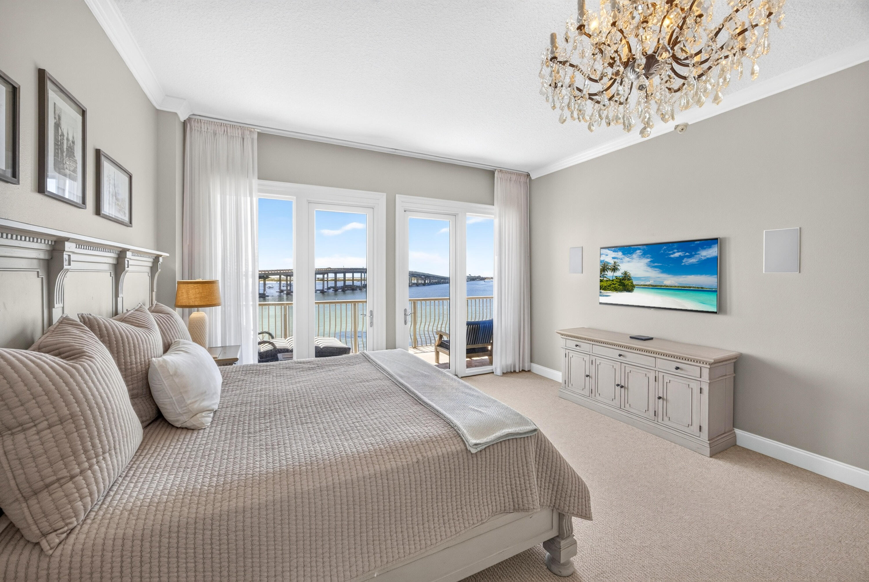 Bedroom with a neutral quilted bed and balcony doors overlooking the water and bridge.