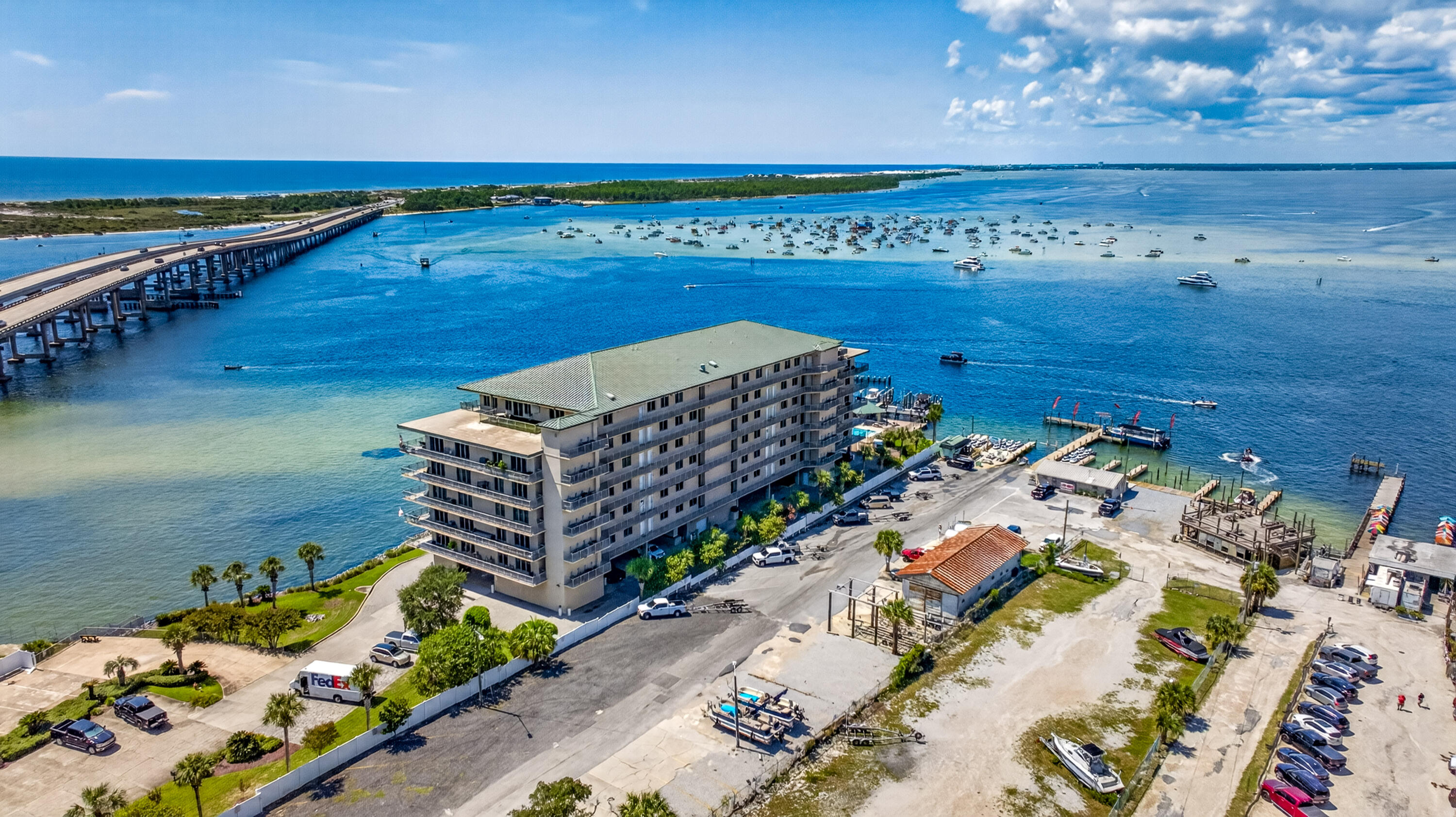Waterfront condominium beside a marina, with boats offshore and a bridge crossing the bay.