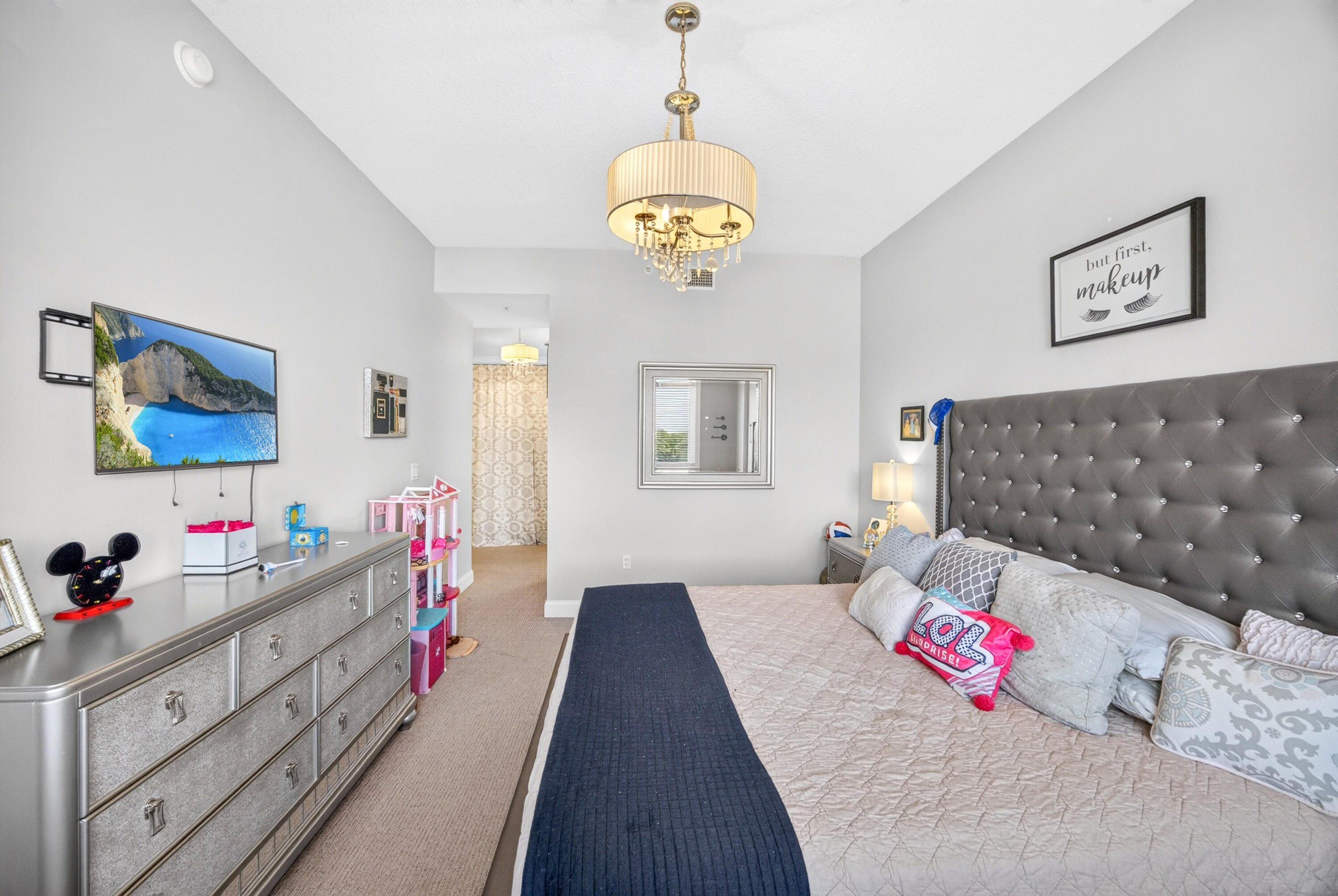 Bedroom with a gray tufted headboard, navy bed runner, silver dresser, and gold chandelier.