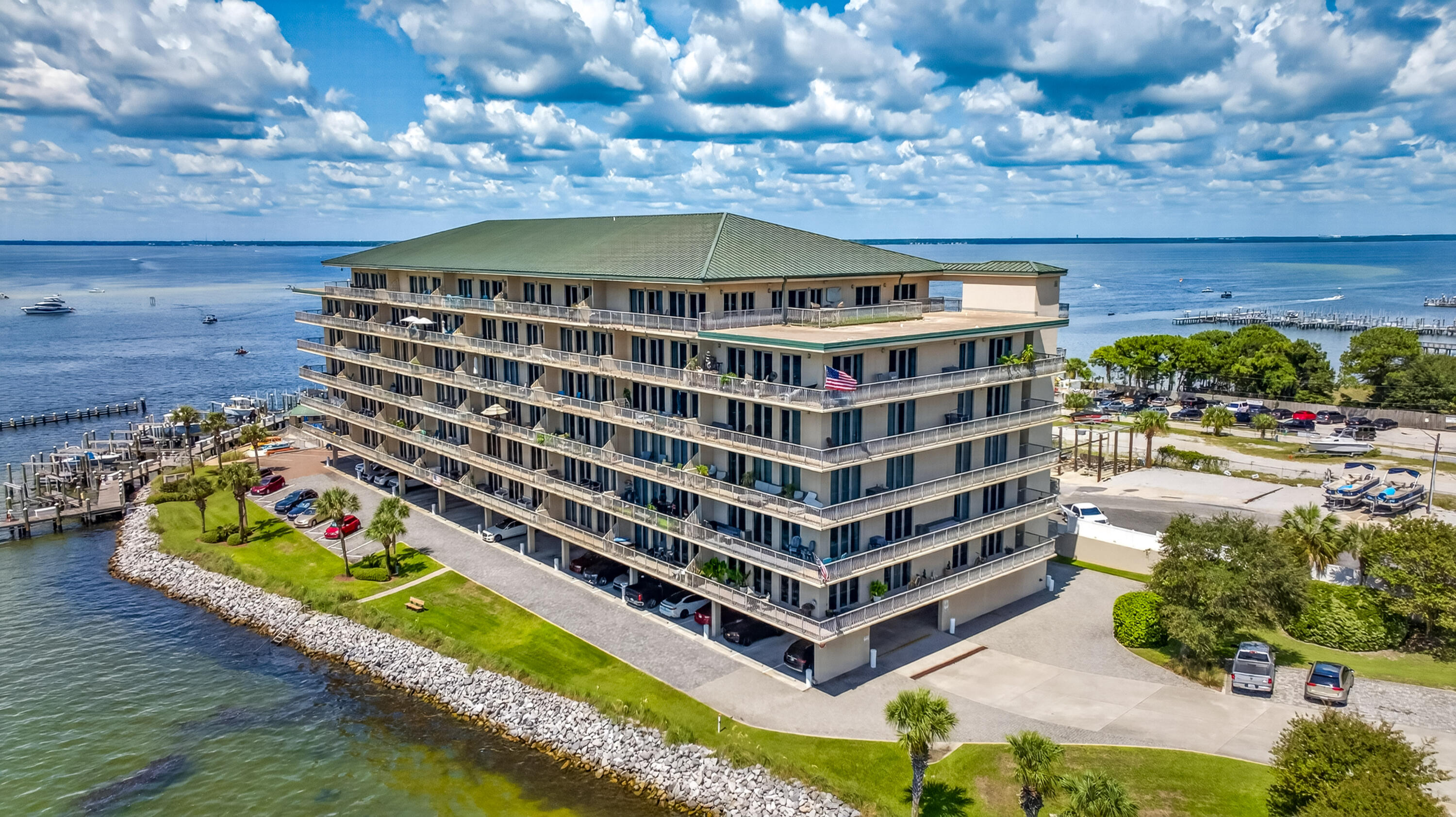 Waterfront condominium with stacked balconies beside a marina and open water.