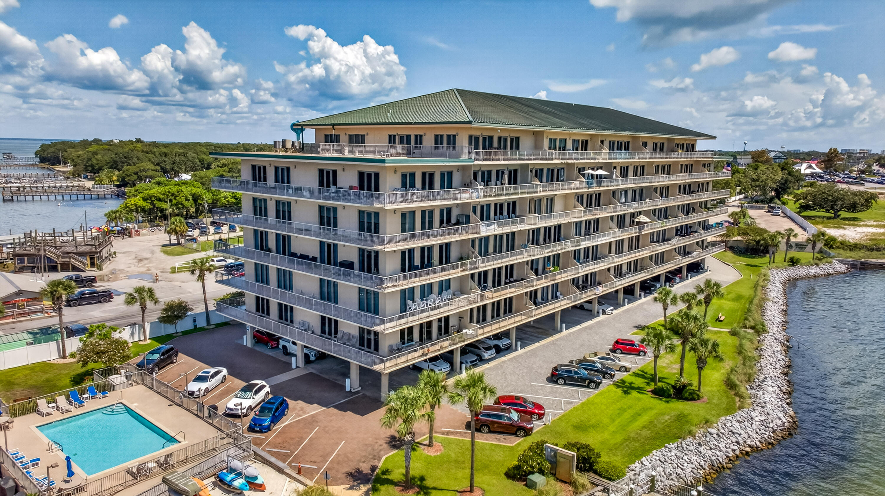 Waterfront condominium with wraparound balconies, a pool, and rocky shoreline.