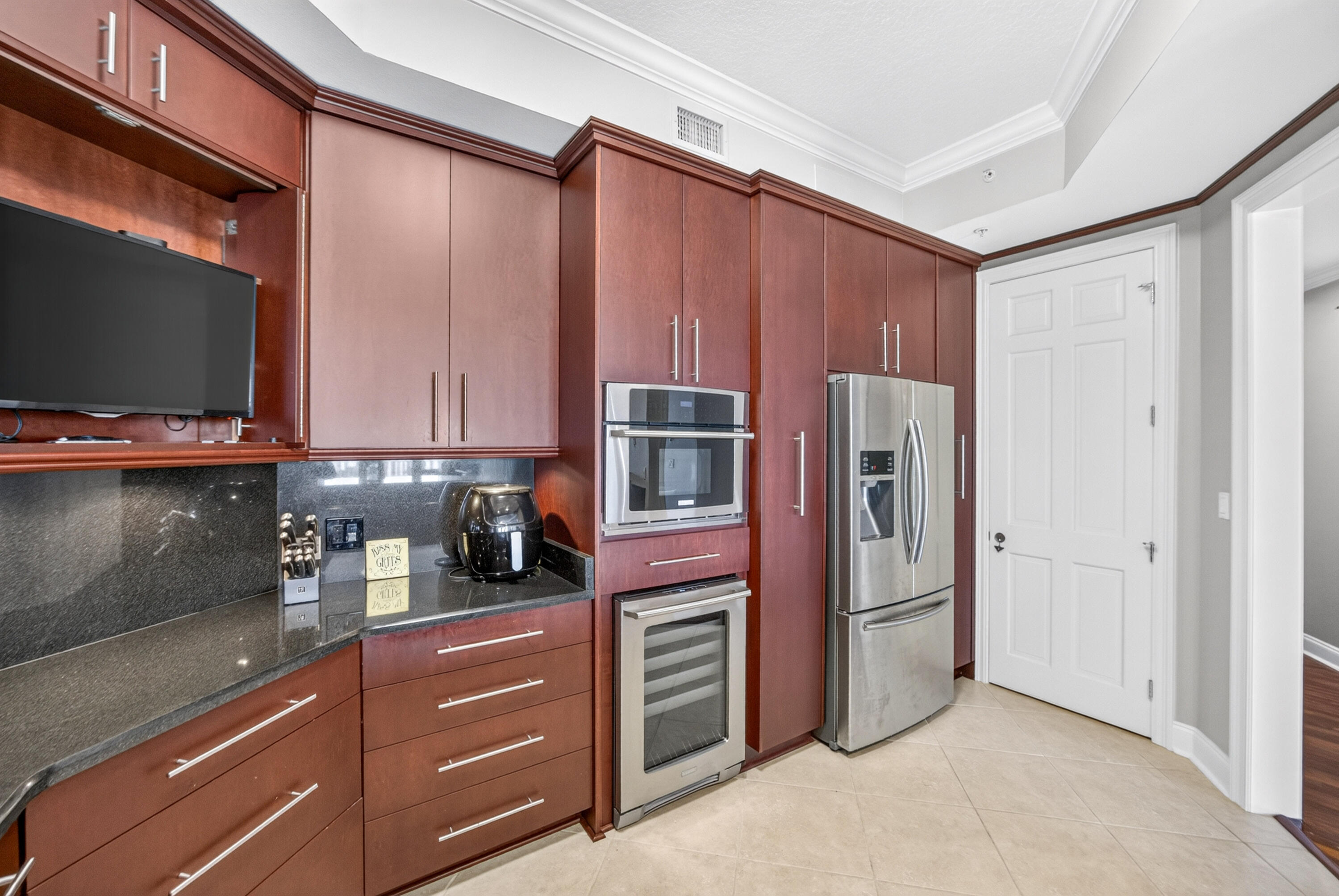 Kitchen with reddish-brown cabinetry, dark stone counters, and stainless-steel appliances.