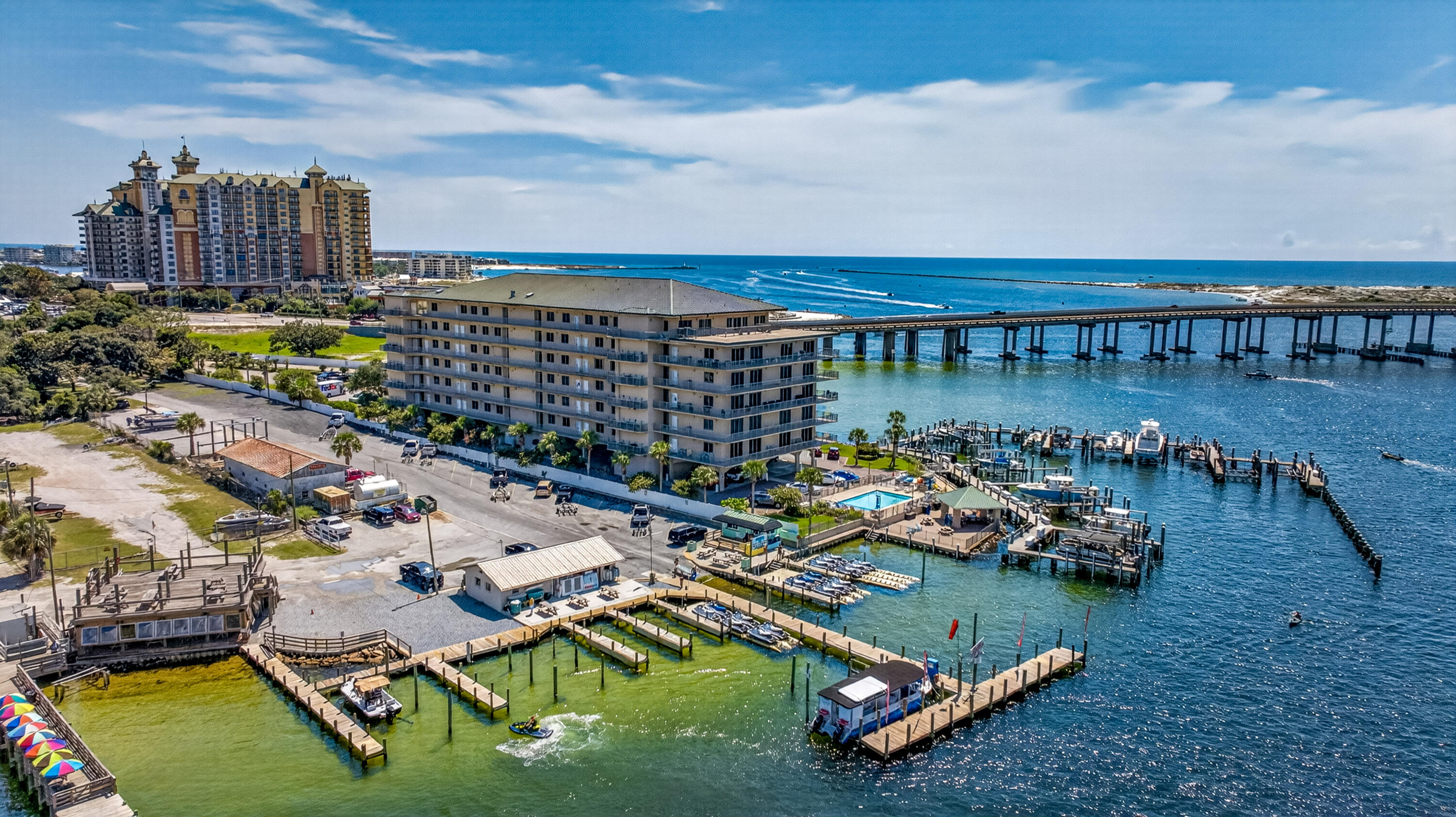 Waterfront condominium beside a marina, with boat docks, a bridge, and the Gulf shoreline beyond.