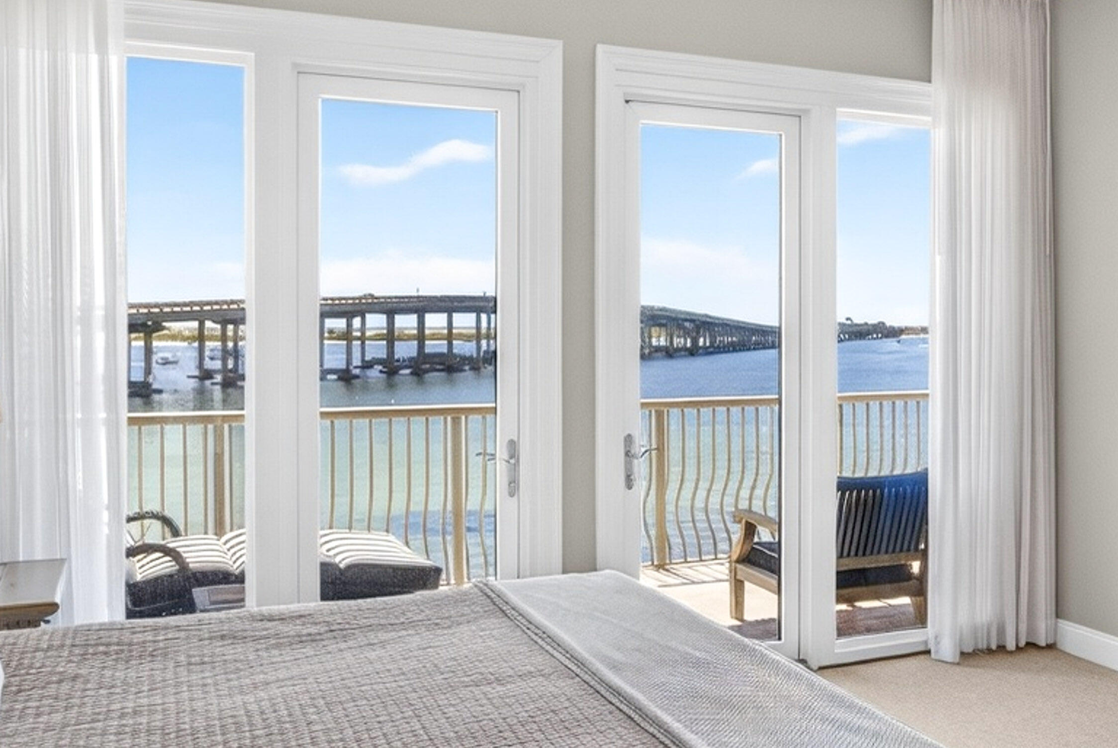 Bedroom with glass balcony doors overlooking the water and a bridge.