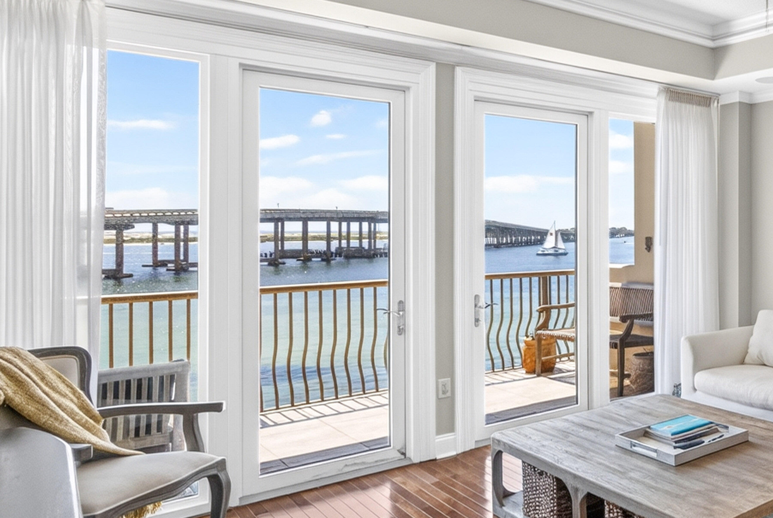 Living room with tall glass doors overlooking a bridge, water, and a sailboat.
