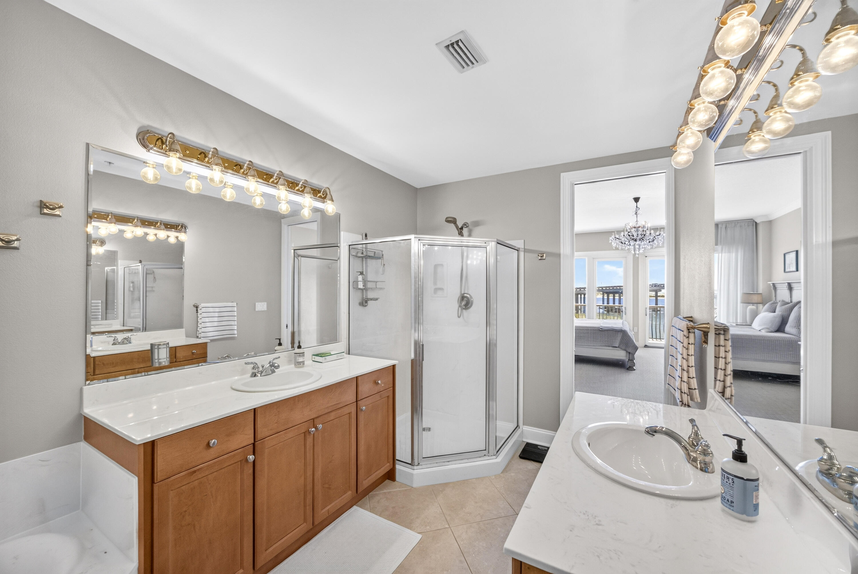 Bathroom with wood double vanity, glass corner shower, and soaking tub beside a bedroom with balcony doors.