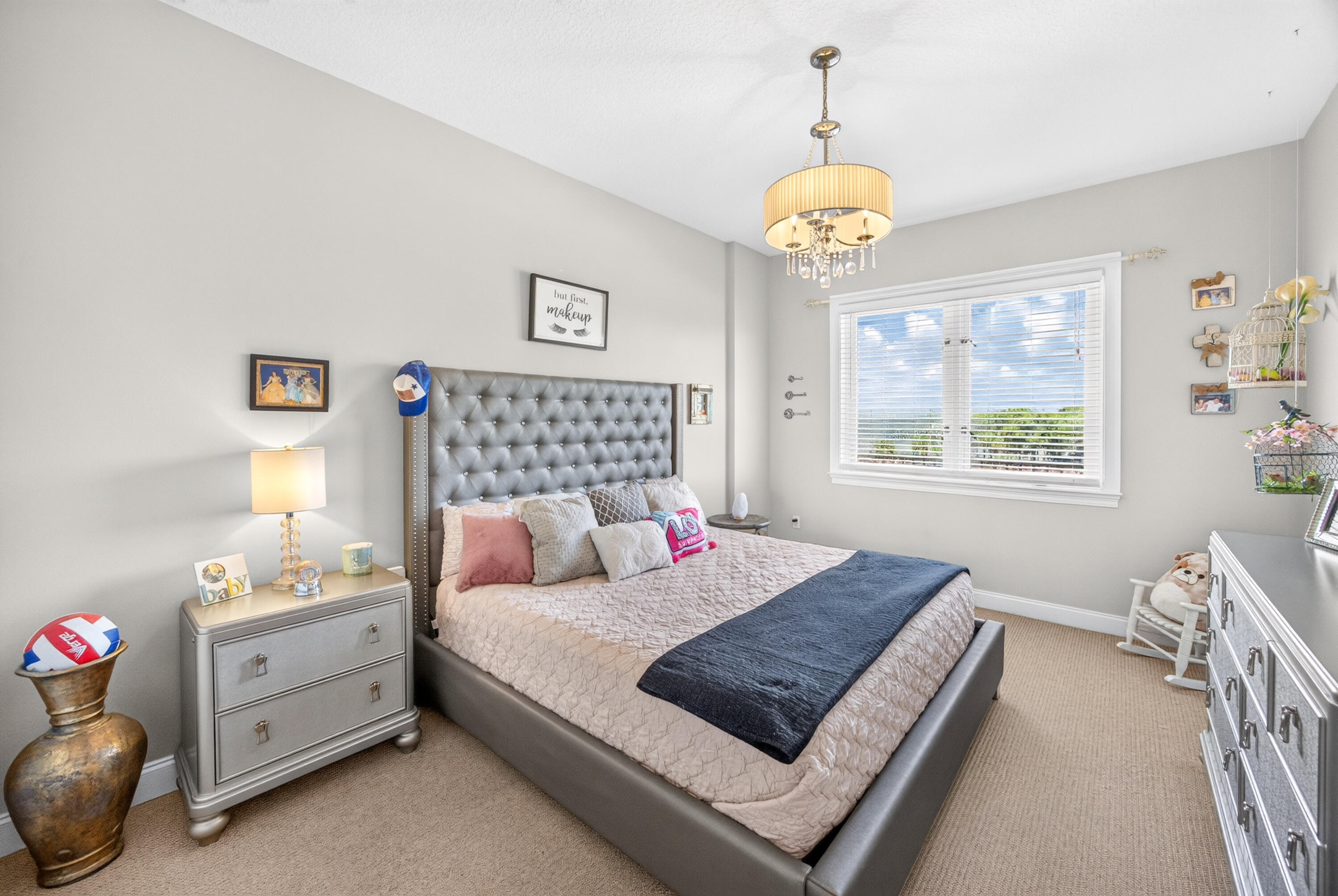 Furnished bedroom with a gray tufted bed, pink bedding, navy throw, and bright window.