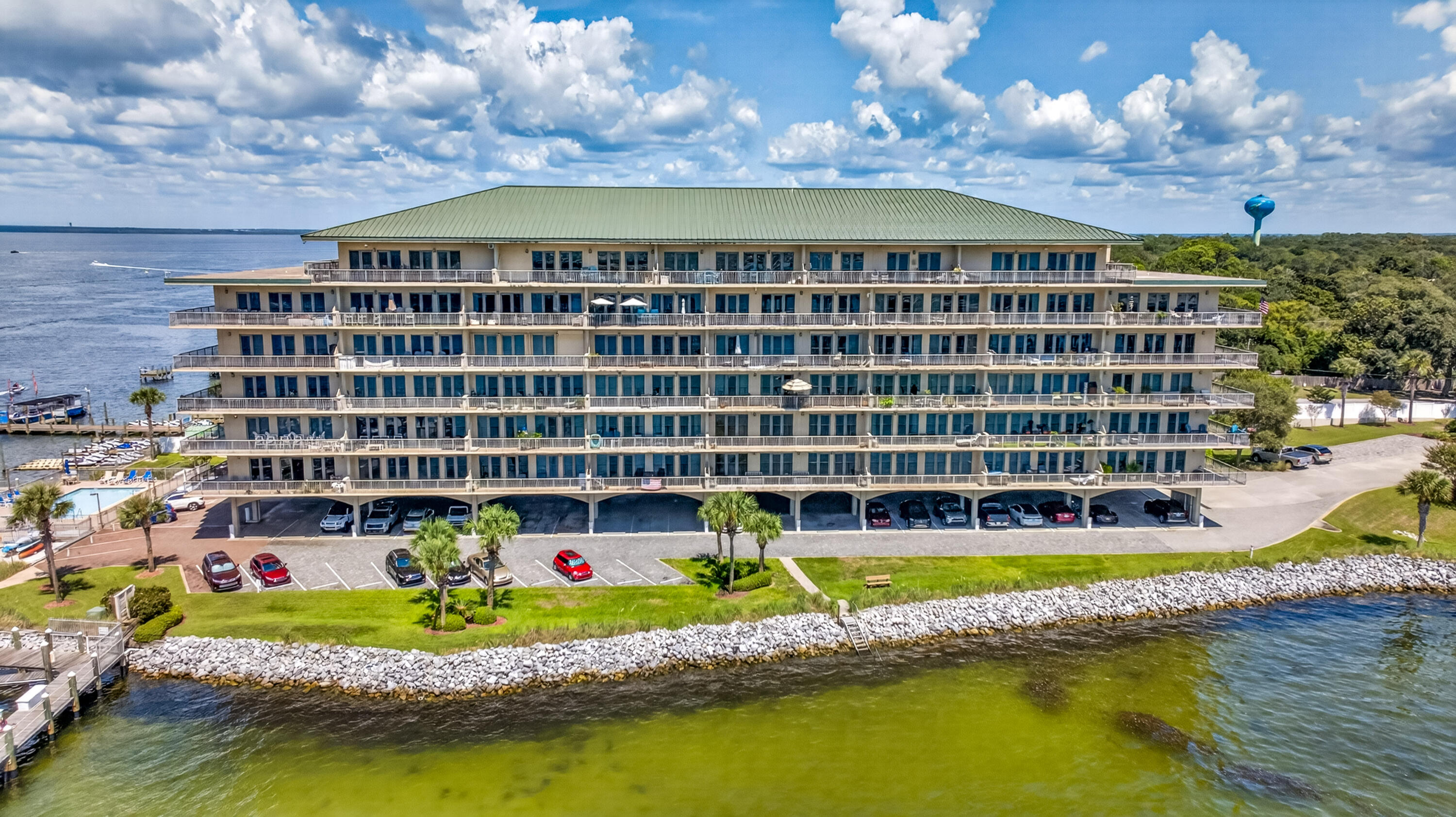 Waterfront condominium with tiered balconies, a green roof, and rocky shoreline.