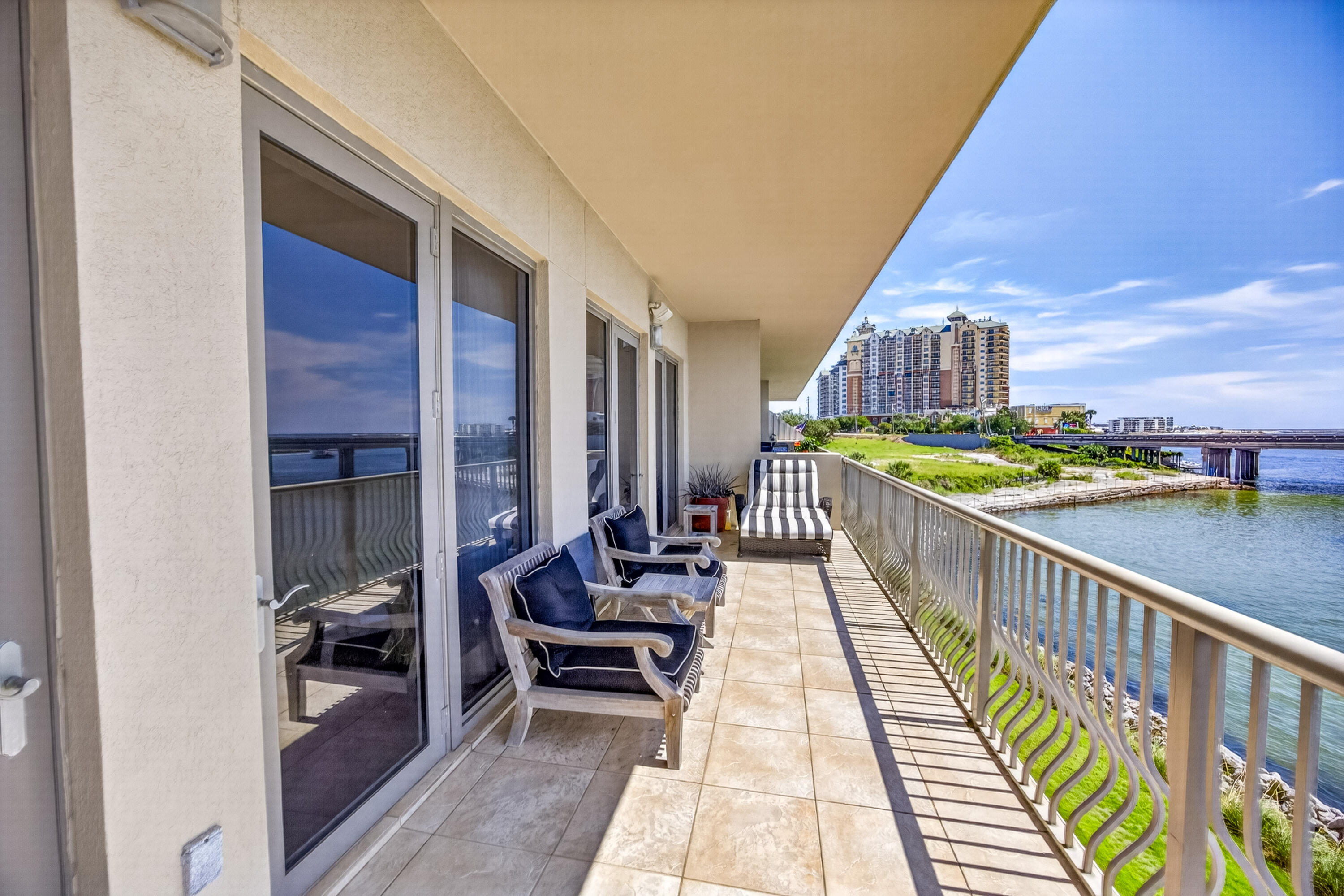 Furnished condo balcony overlooking the water and a bridge, with distant waterfront buildings.
