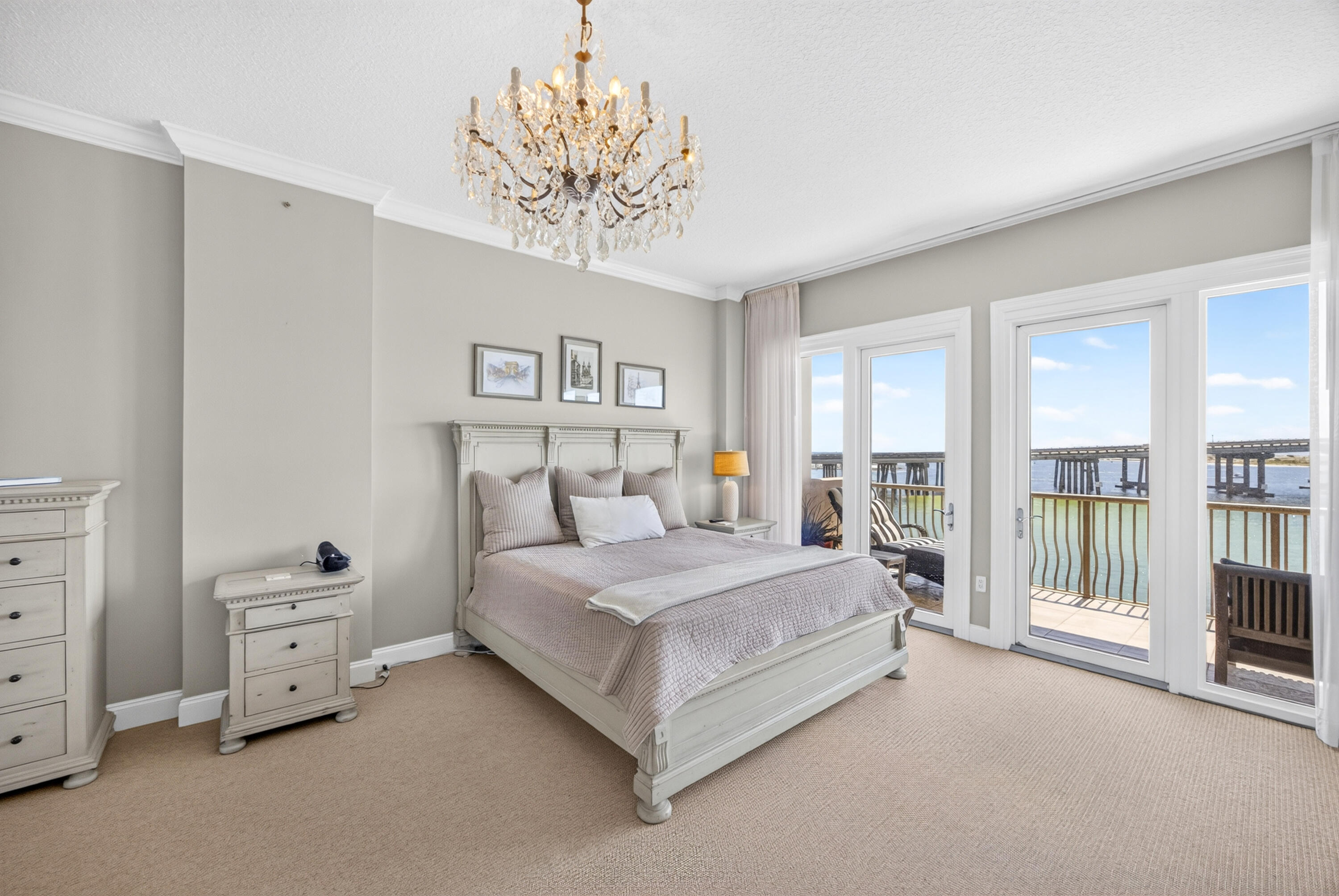 Furnished bedroom with a crystal chandelier and balcony doors overlooking the water and bridge.