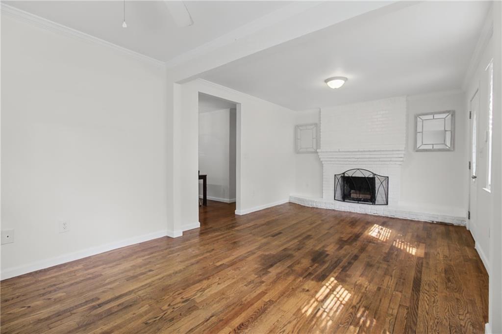 Unfurnished living room with hardwood floors and a white brick fireplace.