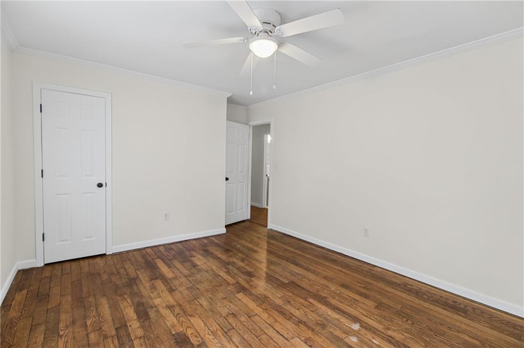 Empty bedroom with hardwood floors and a white ceiling fan.