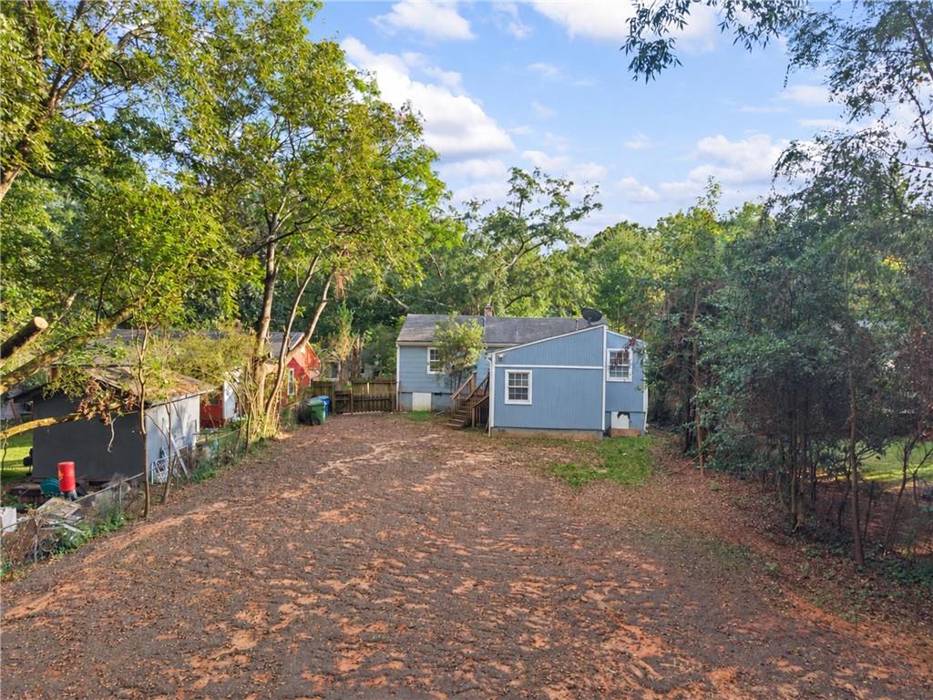 Blue house at the end of a leaf-covered driveway, surrounded by trees and outbuildings.