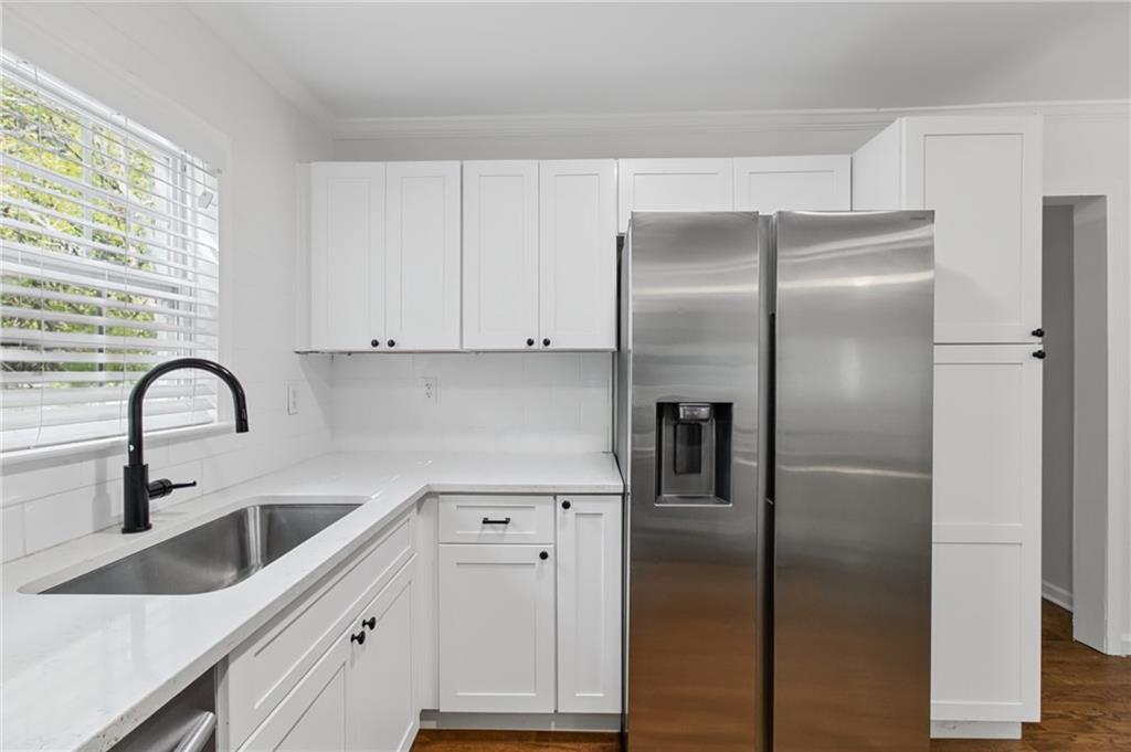 White kitchen with stainless refrigerator, sink beneath a window, and black faucet.