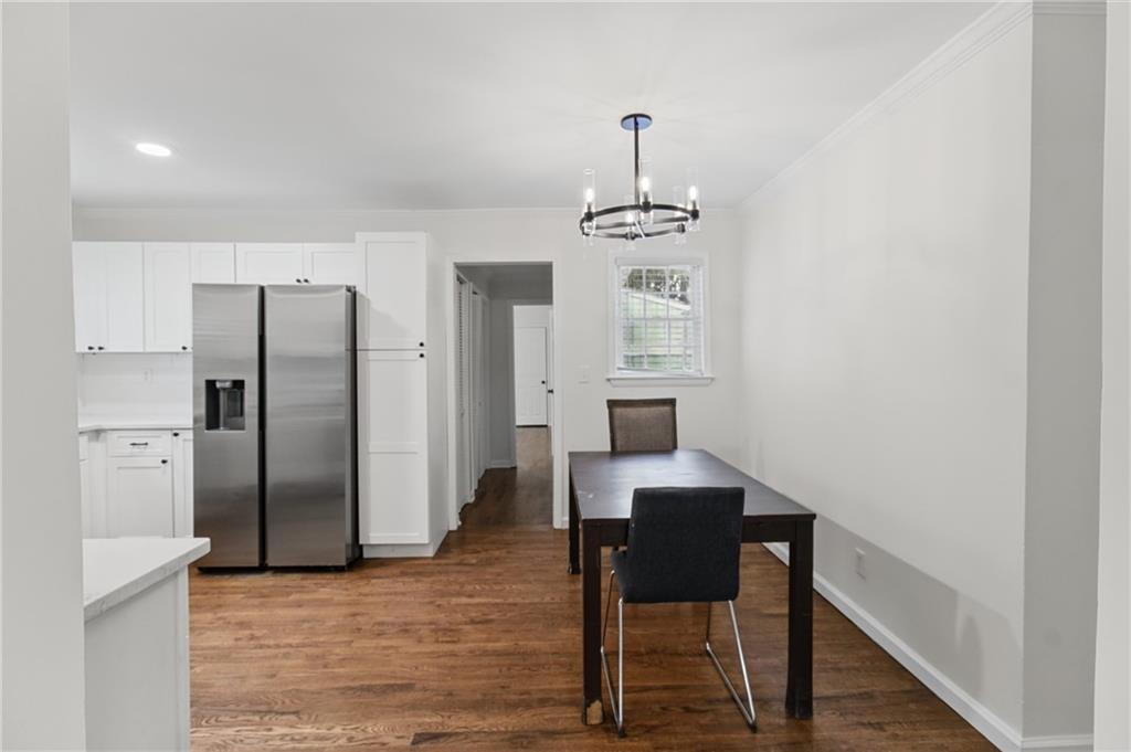 Dining area beside a white kitchen with a stainless refrigerator, dark table, and hardwood floors.