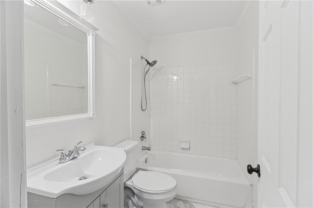 White bathroom with a tiled tub and shower, toilet, and sink vanity beneath a large mirror.
