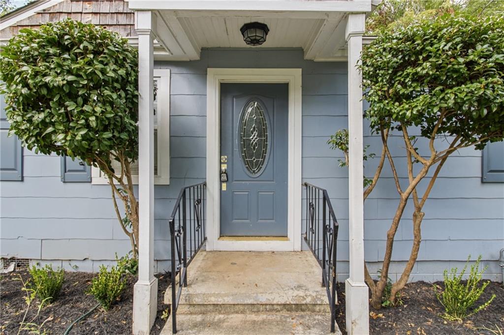 Blue house entrance with an oval-glass door, covered walkway, and trimmed trees.