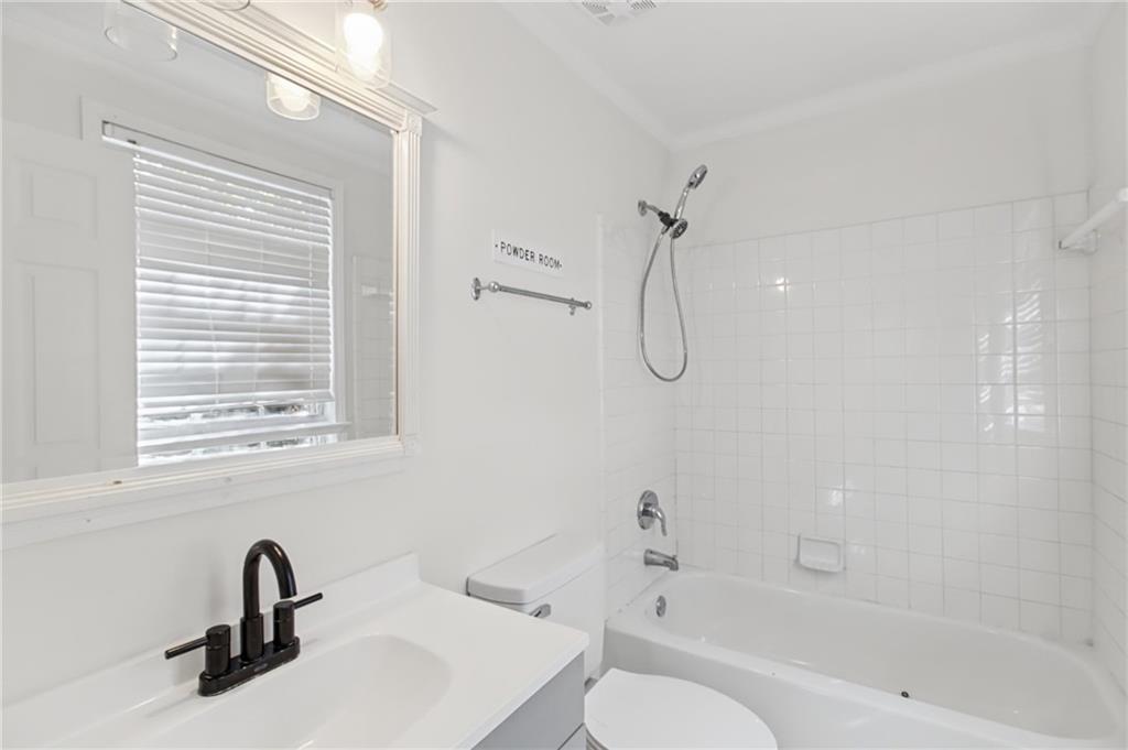 Bathroom with a white tiled tub and shower, vanity, black faucet, and window with blinds.