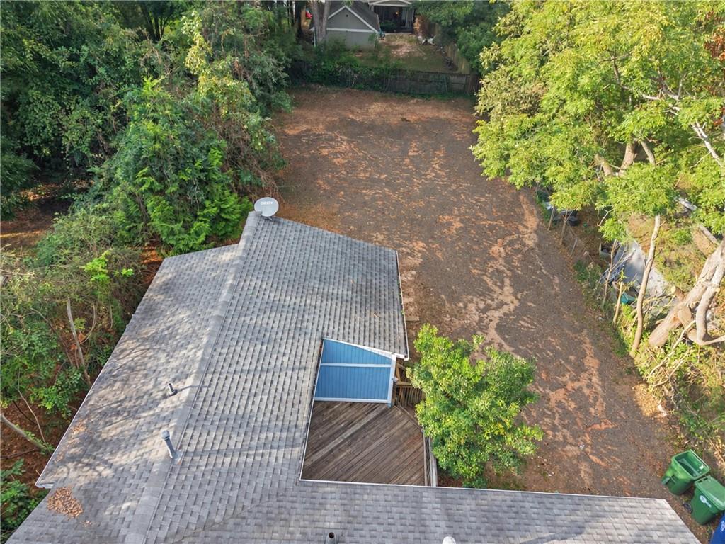 Aerial view of a home’s rear roof and deck beside a broad, tree-lined yard.