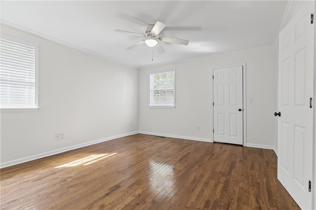 Empty room with hardwood floors, a ceiling fan, and two windows.