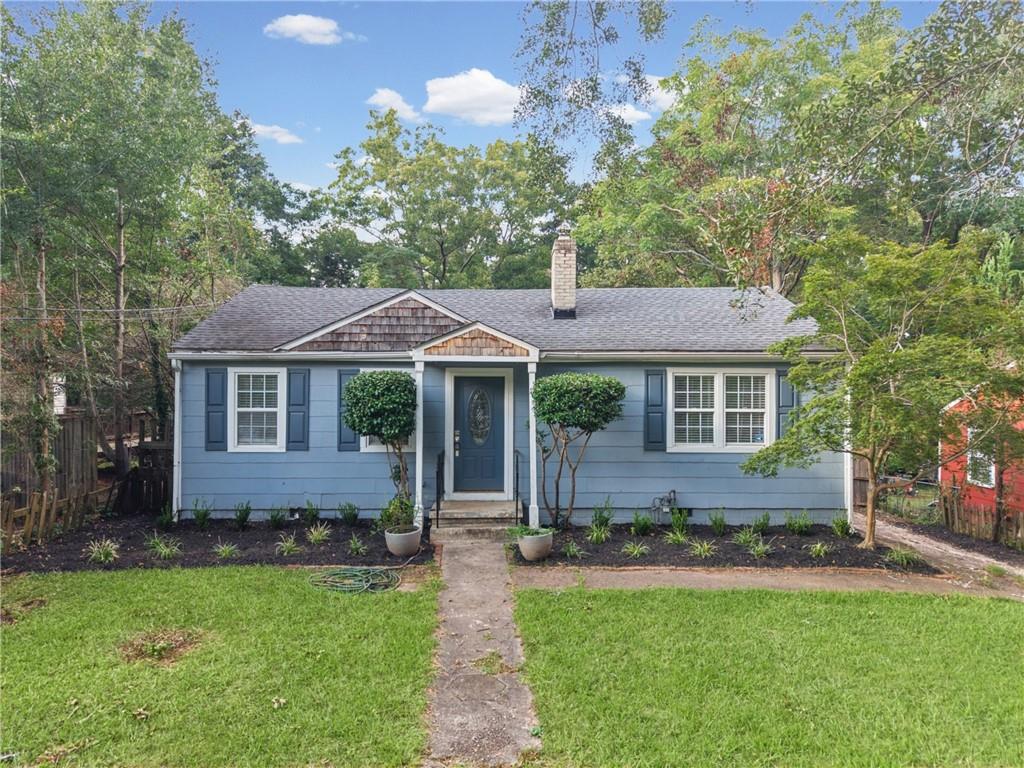 Blue single-story house with dark shutters, a brick chimney, and a walkway through the front lawn.
