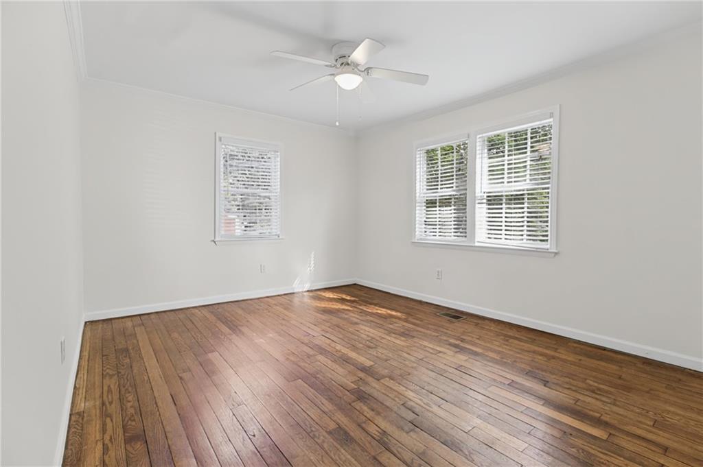 Vacant room with hardwood floors, white blinds, and a ceiling fan with light.