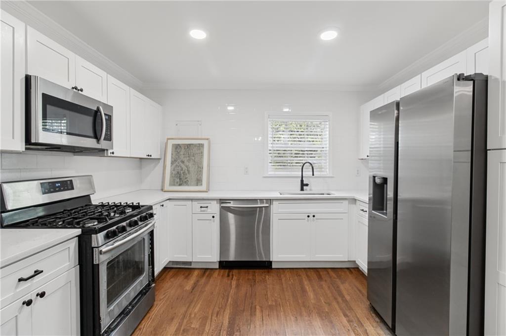 White kitchen with stainless steel appliances, a gas range, and warm wood flooring.
