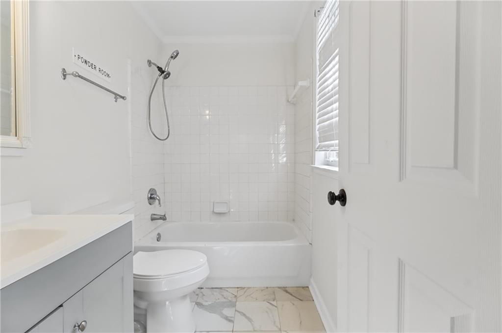 Bathroom with a white tub and tiled surround, vanity, toilet, and marble-patterned floor.