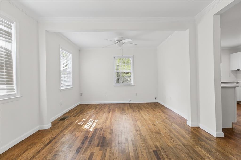 Empty living room with polished hardwood floors, shuttered windows, and a ceiling fan.