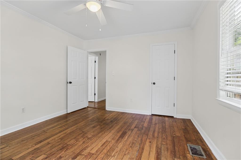 Empty bedroom with hardwood floors, a ceiling fan, and a window with blinds.