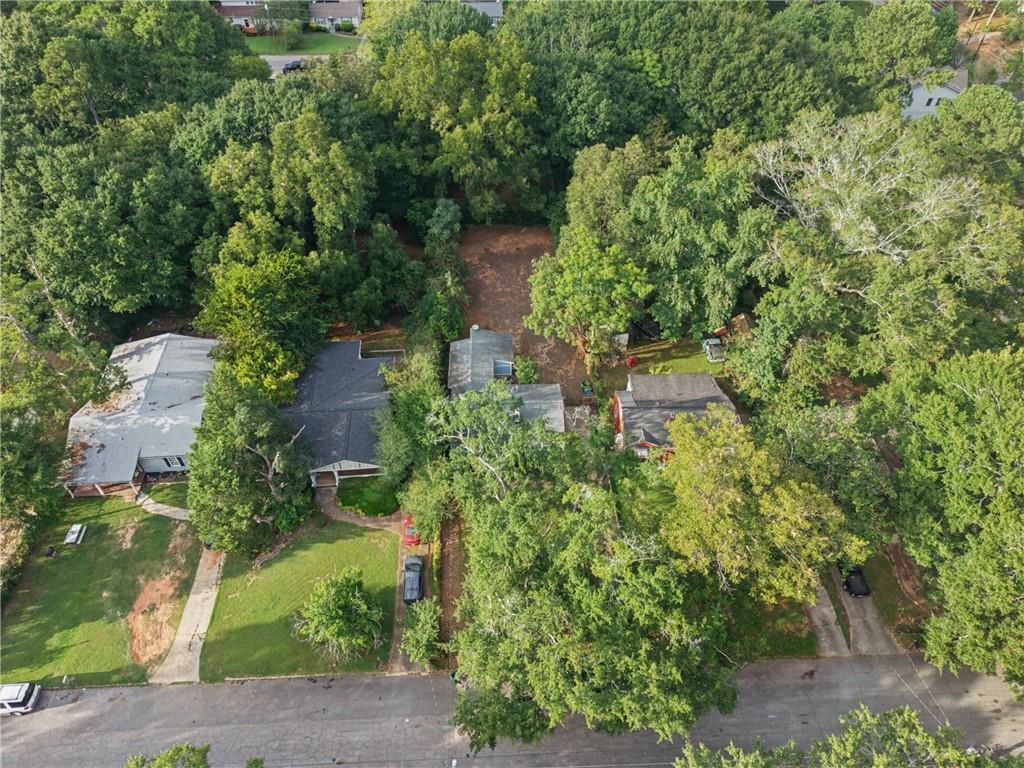 Aerial view of a house surrounded by mature trees, with a wooded backyard and residential street.