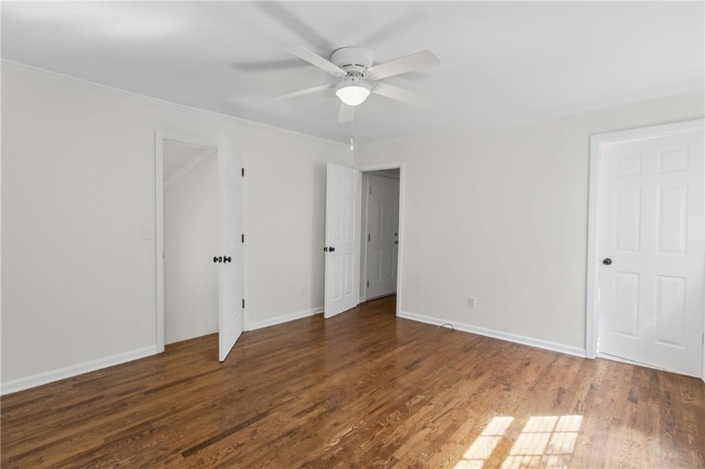 Empty bedroom with hardwood floors, a ceiling fan, and sunlight across the floor.