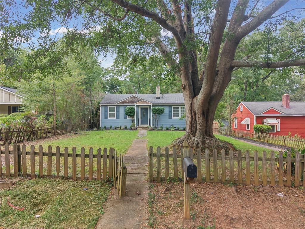 Blue single-story house behind a picket fence, partly obscured by a large mature tree.