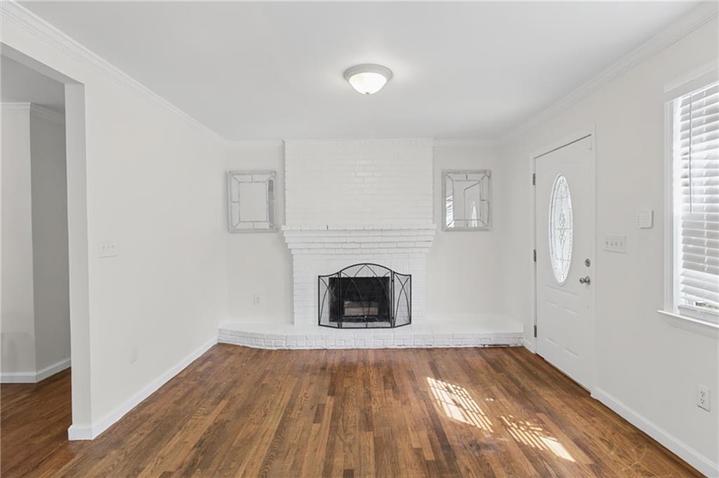 Empty living room with hardwood floors and a white-painted brick fireplace.