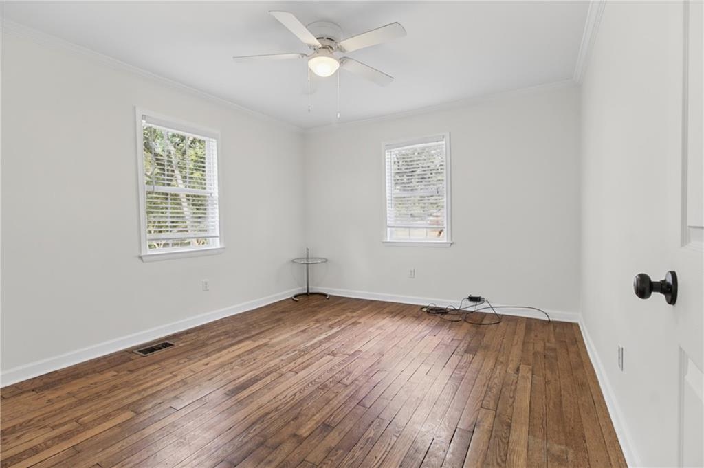 Empty bedroom with hardwood floors, two windows, and a ceiling fan.